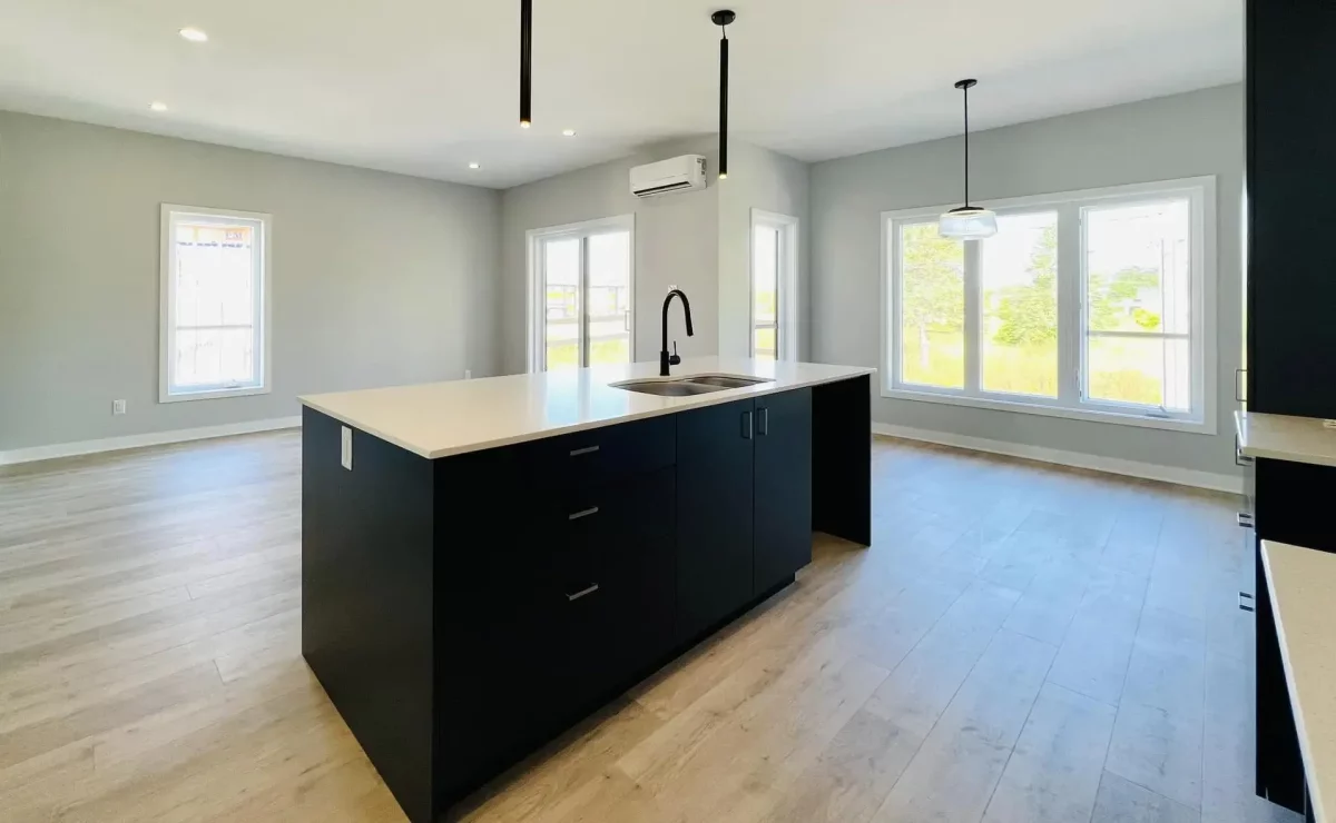 Cuisine à aire ouverte avec îlot noir, comptoir blanc et grandes fenêtres – logement neuf Les Colibris par BGC