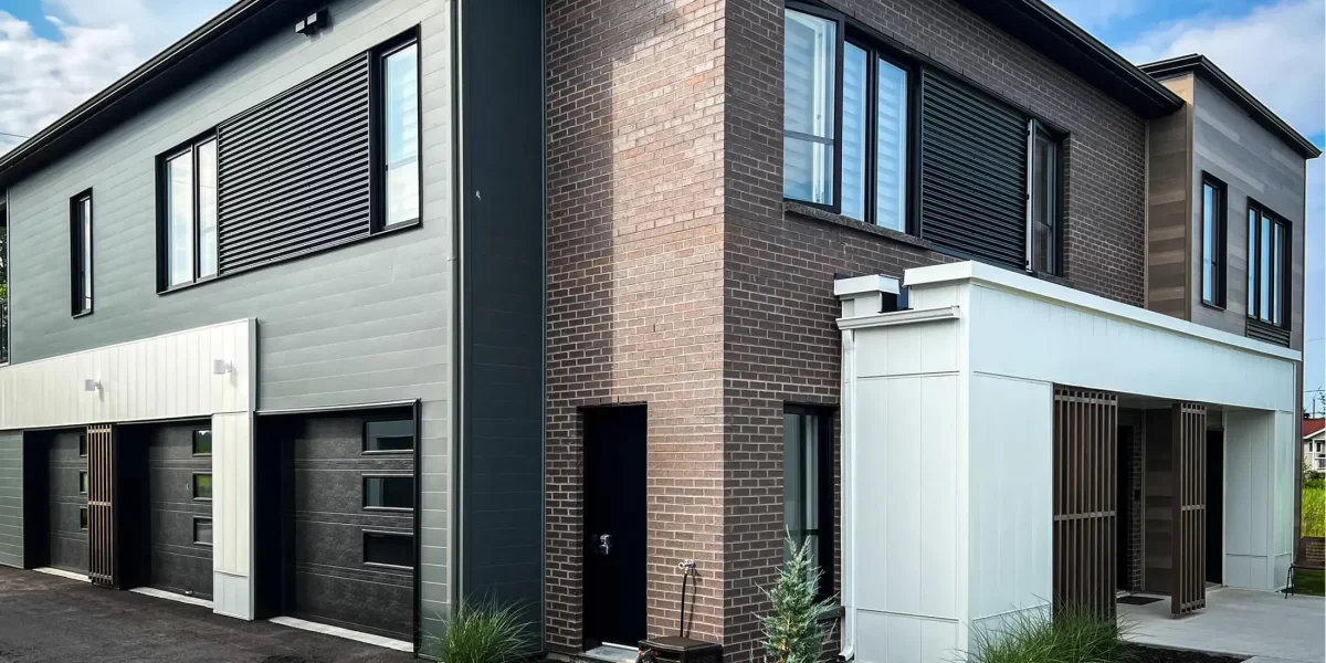 Façade arrière avec portes de garage et revêtements variés briques et bois – construction multi-résidentielle BGC