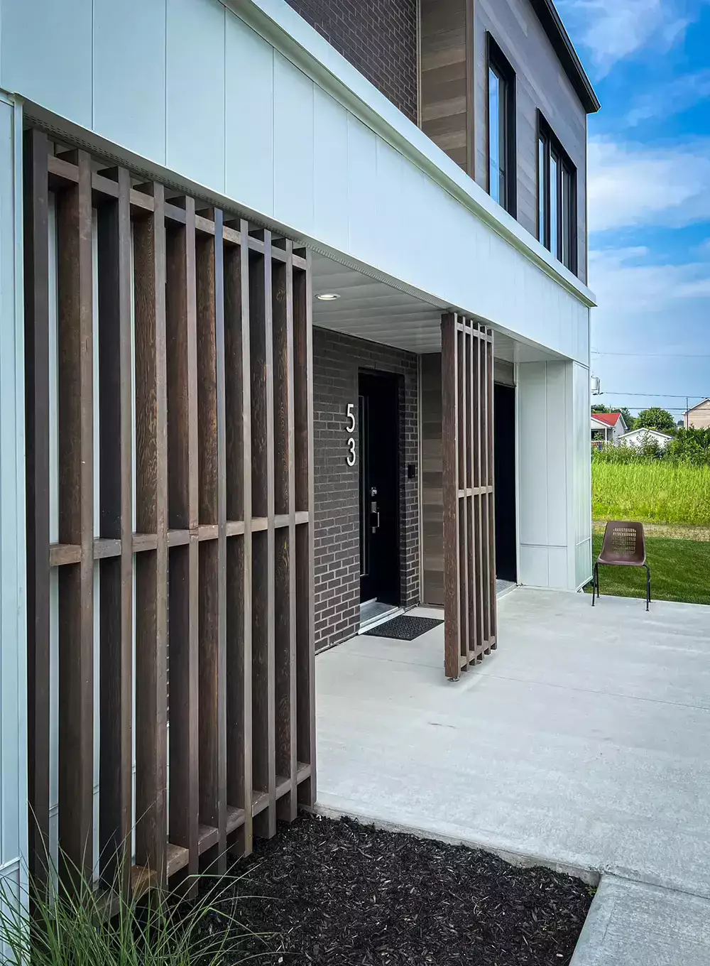 Porche d'entrée avec structure verticale en bois et briques foncées – triplex moderne Les Colibris Joliette