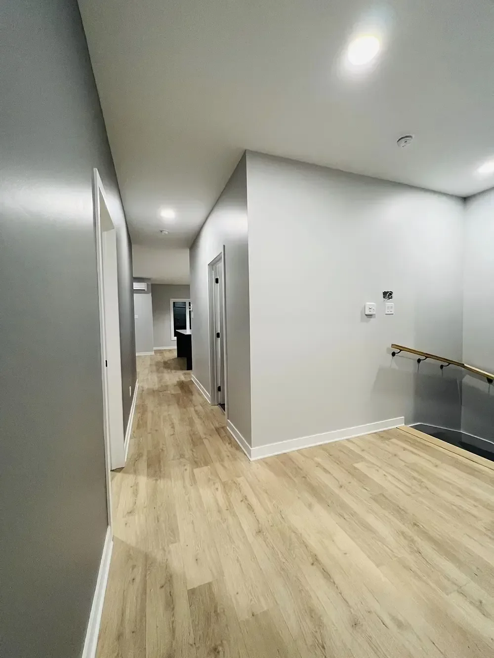 Corridor avec plancher de bois clair, murs gris et escalier moderne – intérieur luxueux Les Colibris par Gestion BGC