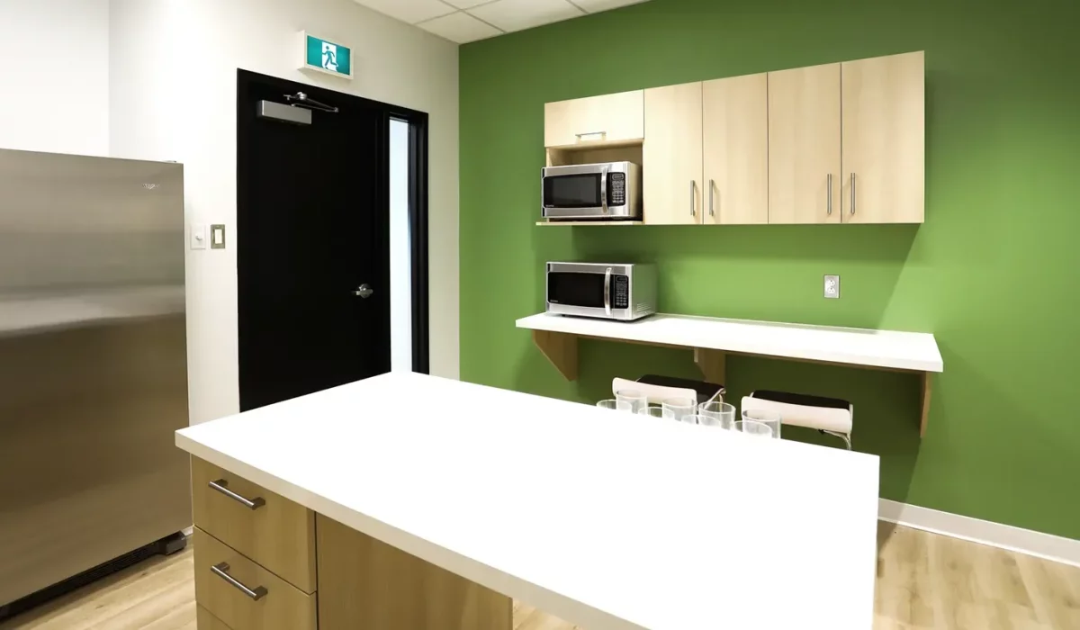 Cuisine des employés avec îlot blanc, mur vert et électroménagers – projet institutionnel Desjardins par Gestion BGC