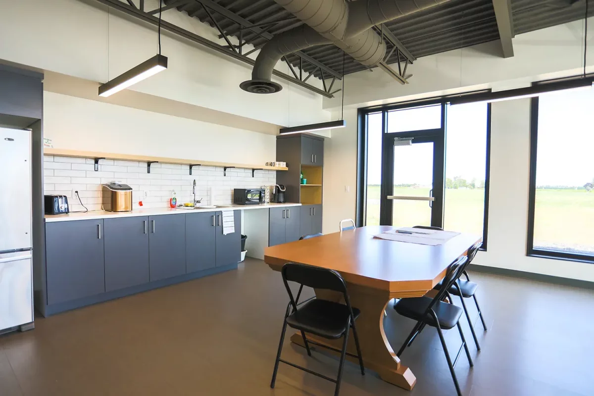 Salle de repos avec armoires grises et grande table en bois – bureaux Jardins Brunelle construction agricole