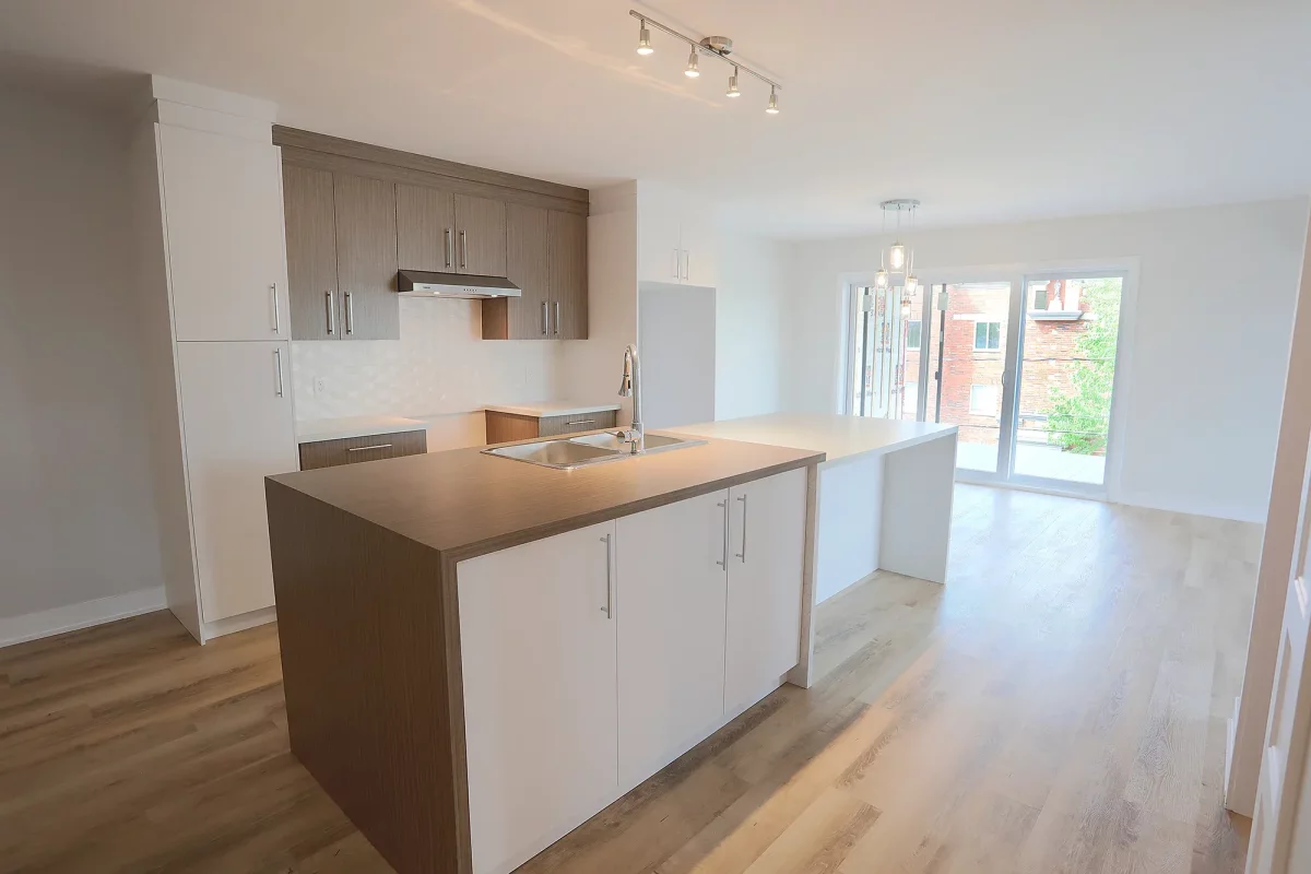 Cuisine avec armoires brunes, comptoirs blancs et plancher de bois – logement neuf Ratelle & Ratelle Joliette