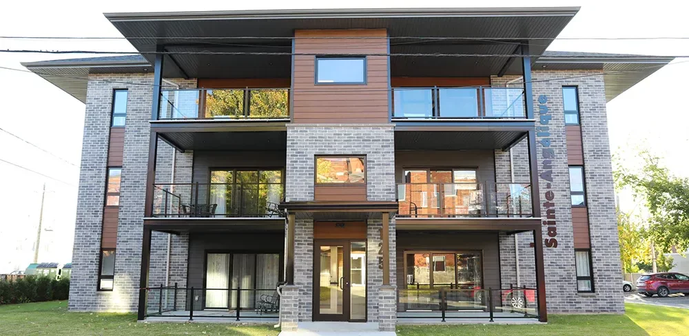 Entrée de l'immeuble Ratelle & Ratelle avec façade de brique grise, balcons noirs et accents de bois – Joliette Lanaudière