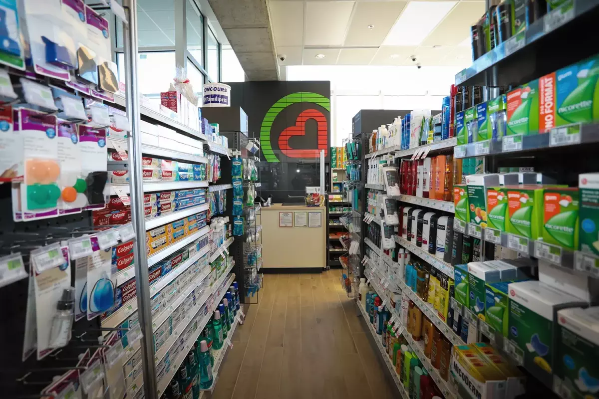 Allée centrale avec grand logo Familiprix au mur et rayons de produits – projet commercial Joliette par Gestion BGC