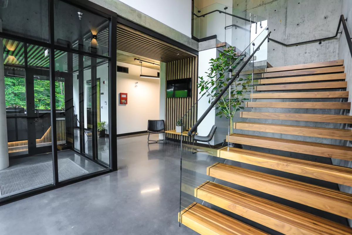 Hall d'accueil avec colonne de béton, coin attente et escalier ouvert en bois naturel