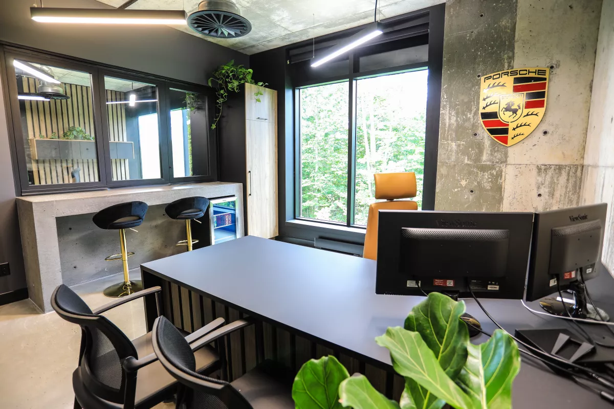 Bureau avec logo Porsche sur mur de béton et luminaires linéaires