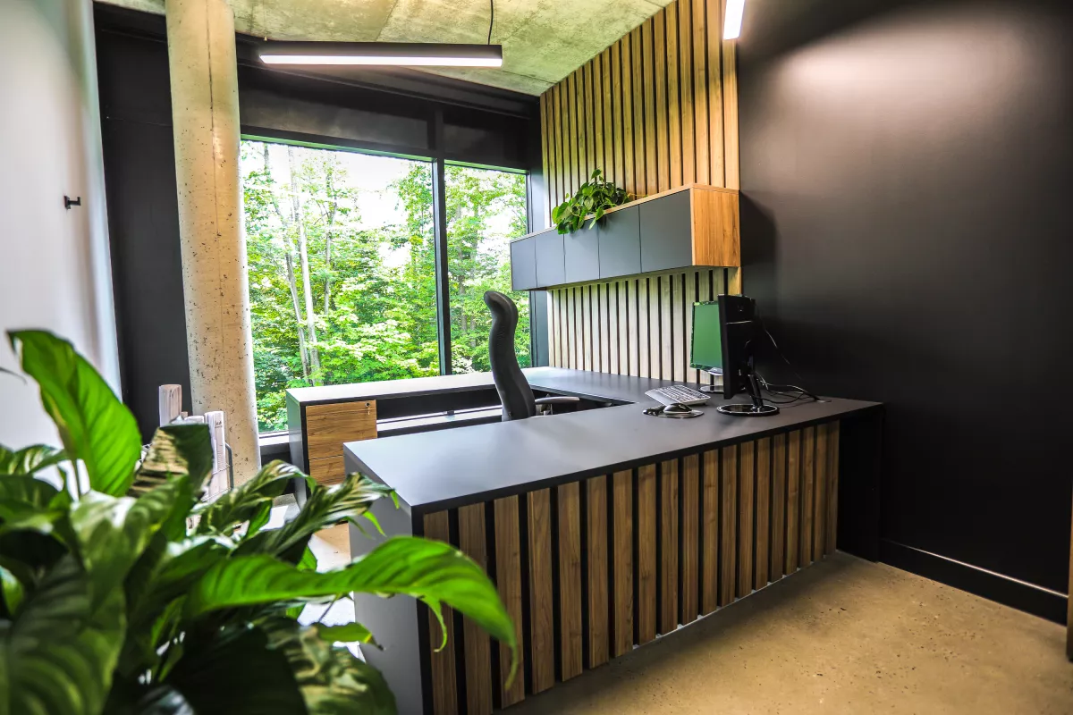 Poste de travail avec bureau en L, murs foncés et grande fenêtre sur la nature