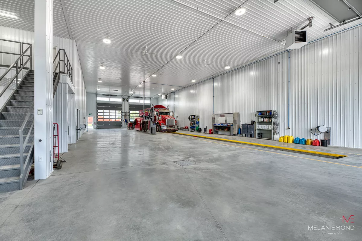 Garage mécanique avec pont élévateur, escalier d'acier et camion rouge – bâtiment industriel Épandage YFL par BGC