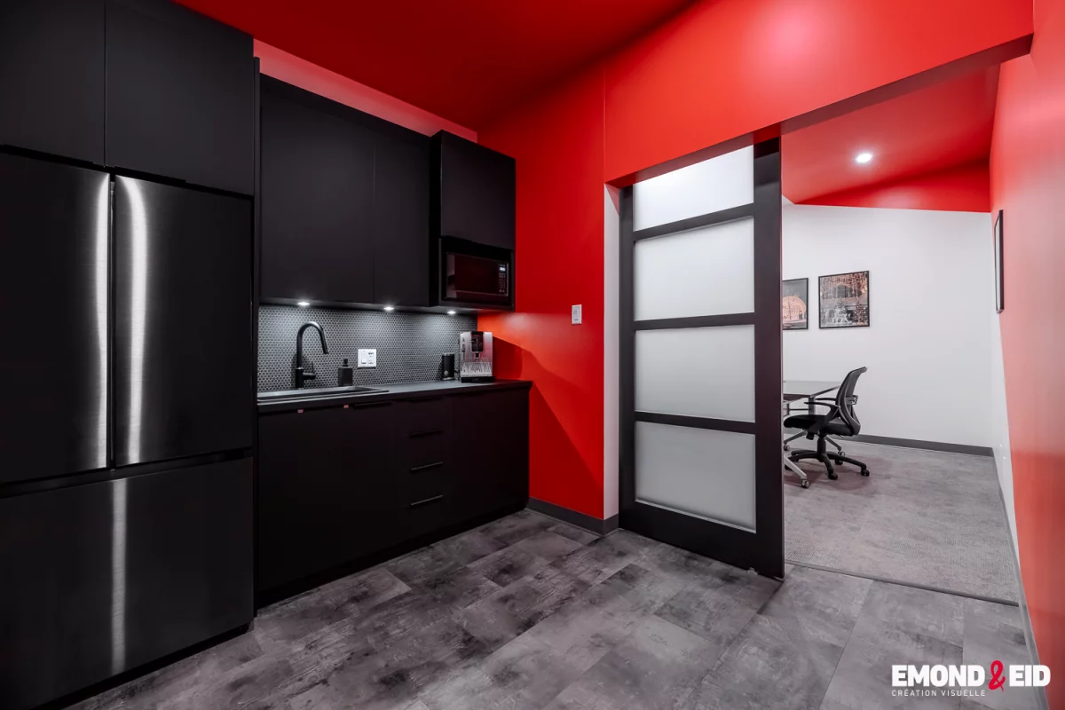 Cuisinette d'entreprise avec armoires noires, mur accent rouge et porte coulissante vitrée