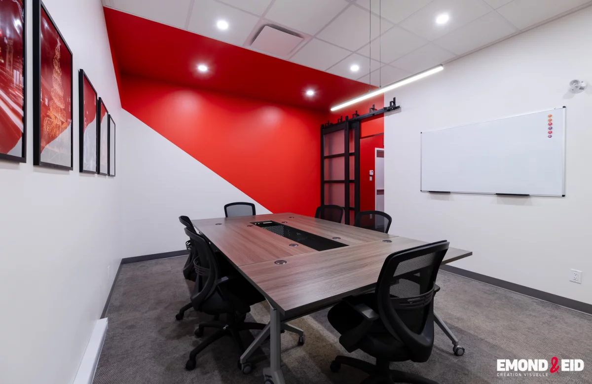 Salle de réunion avec mur accent rouge, cloisons vitrées et tableau blanc