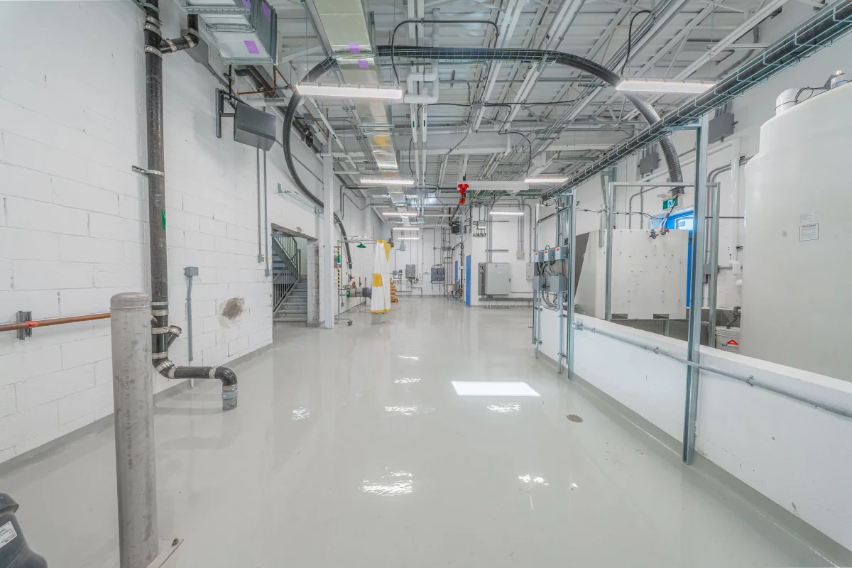 Corridor technique avec conduits apparents, tuyauterie et plancher époxy – construction institutionnelle BGC