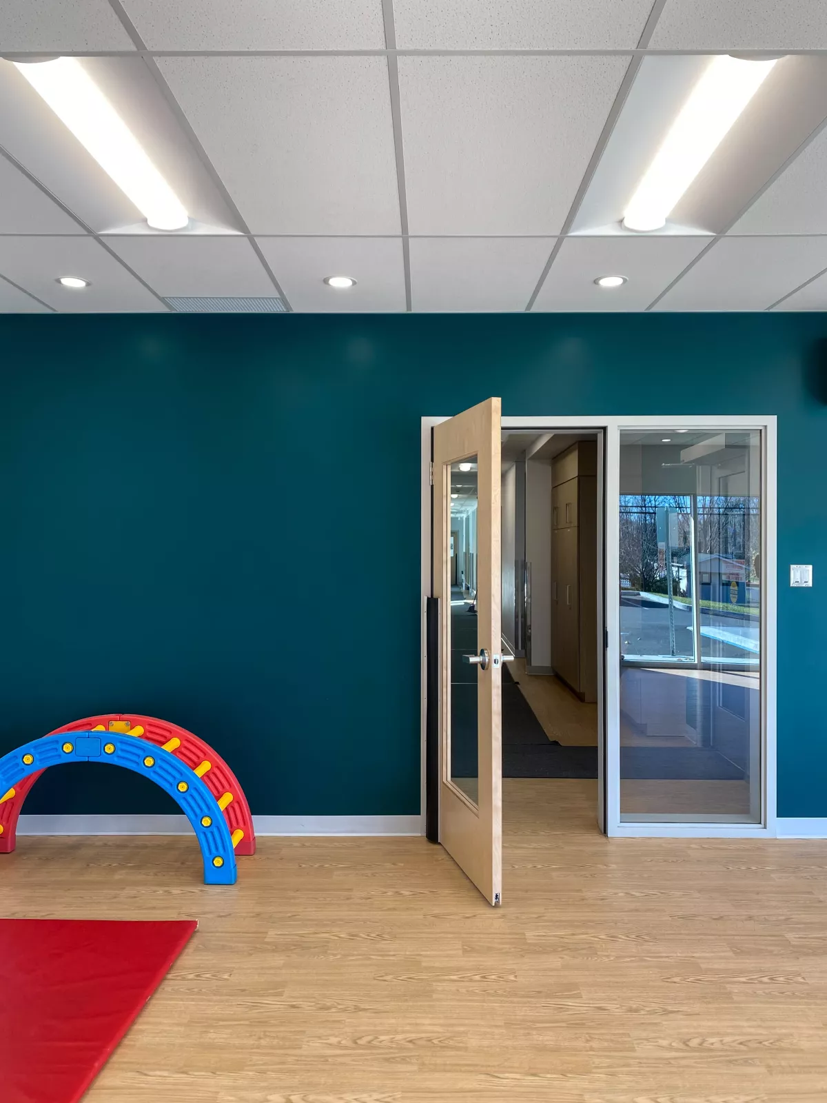 Salle de motricité avec mur bleu sarcelle, plancher de bois et équipements de jeu