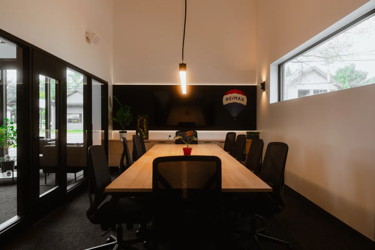 Salle de conférence avec logo RE/MAX, table en bois et mur accent noir