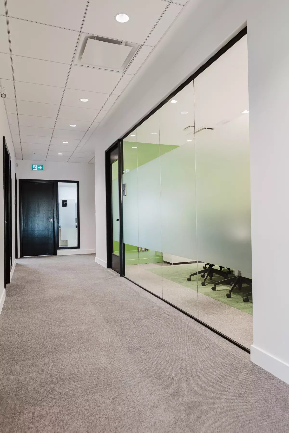 Corridor avec tapis gris et salle de réunion vitrée avec mur accent vert – Desjardins par BGC Lanaudière